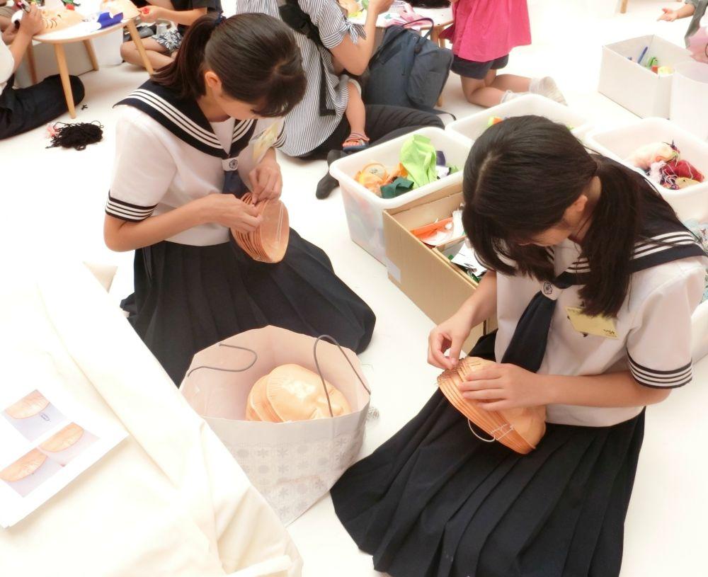 あそびのじかん展の展示会場で中学生がお面にクリップをつけている様子